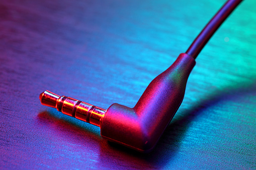 Black AUX audio cable in abstract color lighting, close-up.