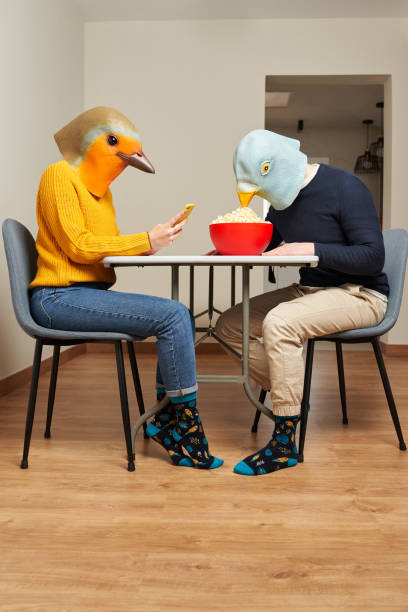 Couple dressed in bird masks eat popcorn at the table