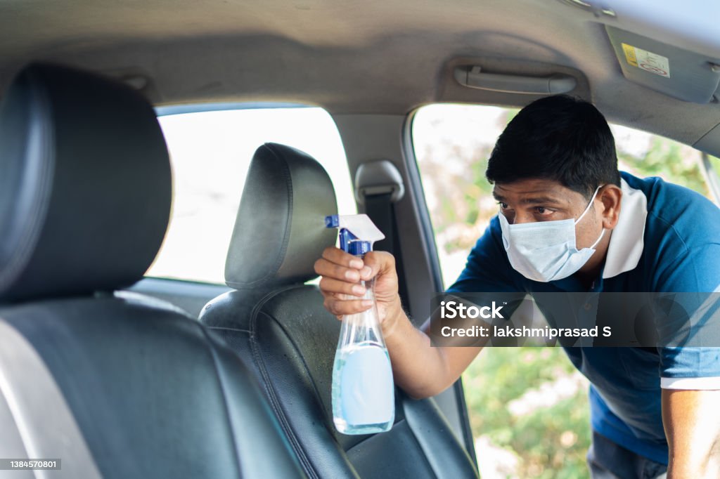 cab or car taxi driver with medical face mask sanitizing passenger seat - concept of coronavirus covi-19 safety measures, hygiene and medical protuction cab or car taxi driver with medical face mask sanitizing passenger seat - concept of coronavirus covid-19 safety measures, hygiene and medical production. Car Stock Photo