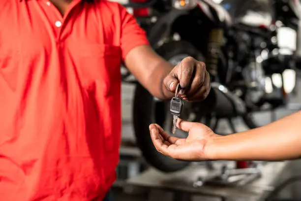 Close up of bike mechanic hands giving motorbike key to customer after maintenance service at garage - concept of successful completion repair service.