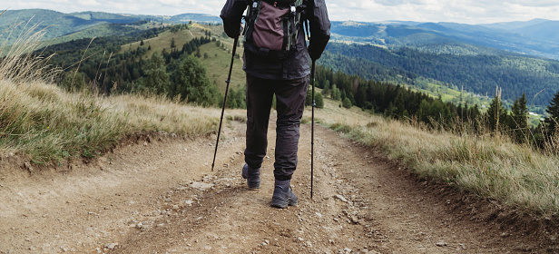 Back view of hiker young man with backpack and trekking poles walking in the mountains