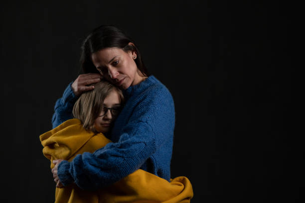 istock Sad mother hugging her daughter, both wearing Ukrainian national colors on black background. 1384580098