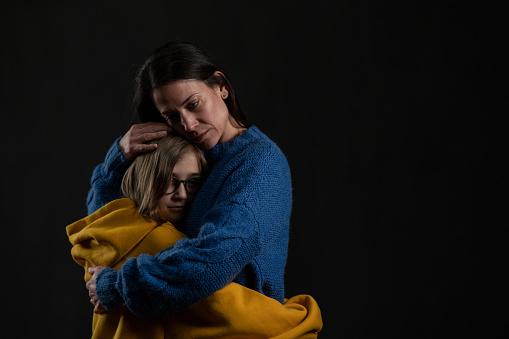 A sad mother hugging her daughter, both wearing Ukrainian national colors on black background.