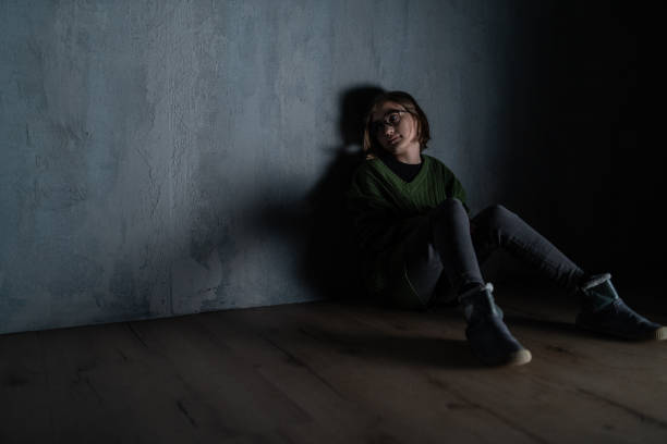 istock Sad little girl, alone in darkness, sitting and thinking. 1384581229