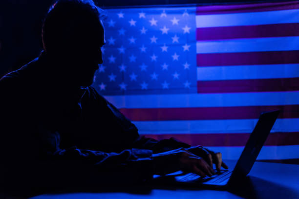 istock Hacker with laptop and USA flag in background. Cyber attack concept. 1384581399