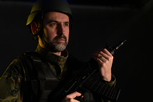 Soldier in military uniform and helmet with weapon on black background.
