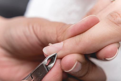 Un manicurista usa un par de pinzas para recortar los bordes y la cutícula y eliminar las uñas colgantes de una uña índice. En un salón o spa de uñas. photo