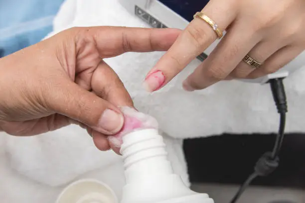 A manicurist uses a cotton bud soaked in acetone to remove leftover polish from the index fingernail of a customer. At a salon or parlor.