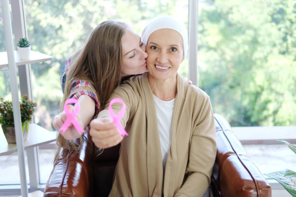 白人の娘は白いヘッドスカーフで高齢の母親にキスは笑顔で、一般的な癌の意識ピンクのリボンを保持することは、乳癌患者のための様々なキャンペーン活動の象徴です。 - senior adult family cheerful couple ストックフォトと画像