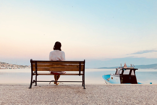 Female model sitting on the bench on the bank of Aegean Sea, Turkey