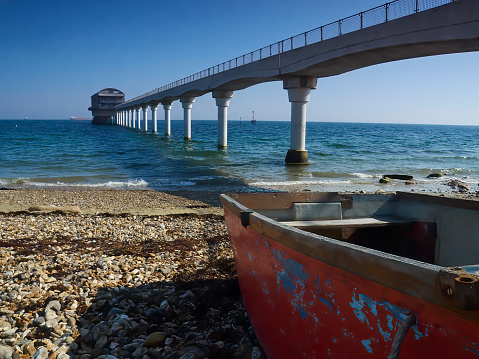 A view from the shade of a derelict boat on the shore at Bembridge, including an expansive blue sky-and-sea, and the local lifeboat station.
