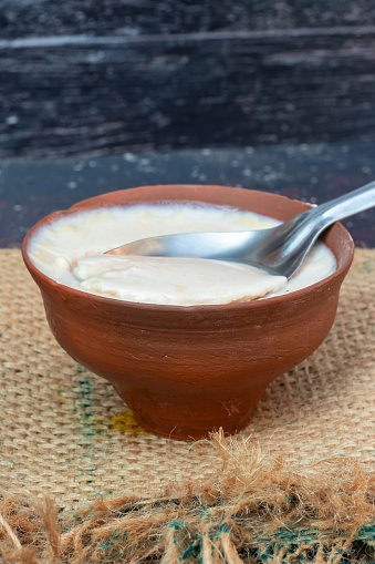 Homemade Dahi or Curd in an Earthen Bowl with Spoon on Burlap Fabric in Vertical Orientation.