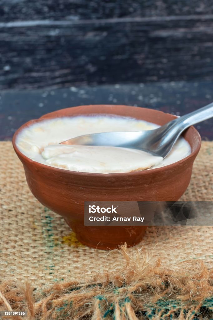 Closeup of Homemade Dahi or Curd in an Earthen Bowl with Spoon on Burlap Fabric in Vertical Orientation Homemade Dahi or Curd in an Earthen Bowl with Spoon on Burlap Fabric in Vertical Orientation. Curd Cheese Stock Photo