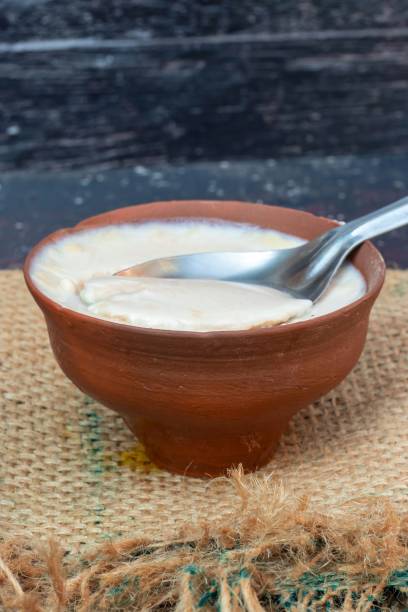 Closeup of Homemade Dahi or Curd in an Earthen Bowl with Spoon on Burlap Fabric in Vertical Orientation Homemade Dahi or Curd in an Earthen Bowl with Spoon on Burlap Fabric in Vertical Orientation. curd cheese stock pictures, royalty-free photos & images