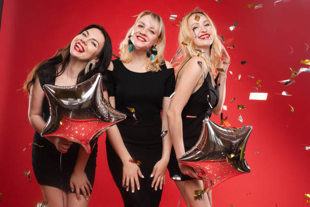 istock Group smiling woman posing surrounded by colorful shimmering confetti isolated red studio background 1384596963