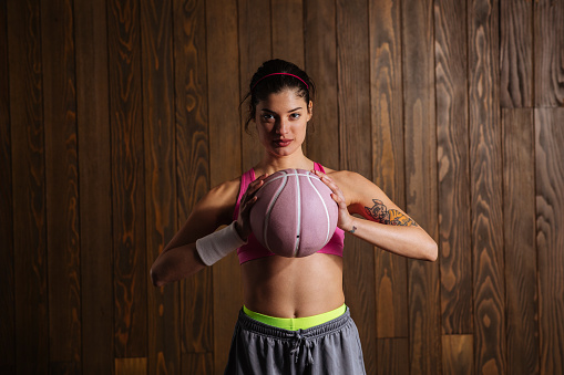 Portrait shot of fit young woman holding basketball indoors