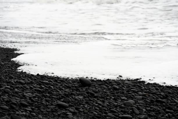 A close-up view of smooth black pebbles glistening with moisture on Reynisfjara Beach, South Iceland. The volcanic stones, polished by the waves of the Atlantic Ocean, create a mesmerizing texture and a deep contrast under the natural light. This famous black sand beach, known for its dramatic landscapes and geological formations, offers a unique perspective of Iceland’s rugged coastline