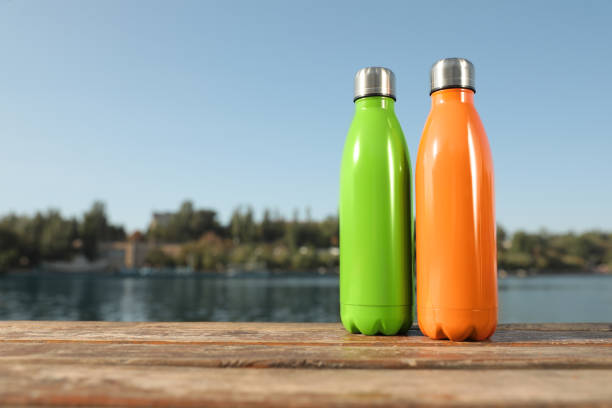 istock Modern thermoses on wooden surface near river. Space for text 1384610006