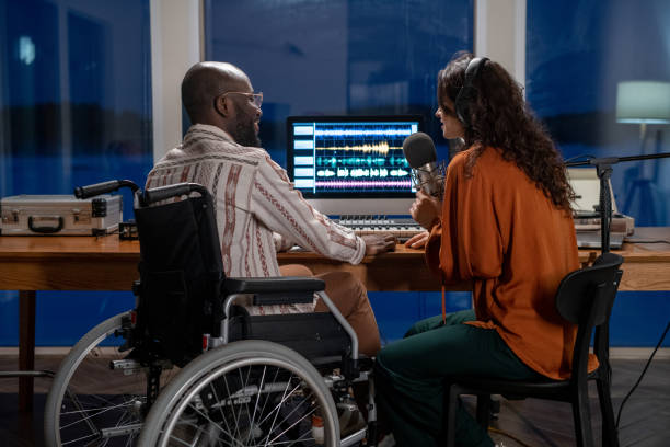 Young African American man in wheelchair looking at female singing in microphone Young African American man in wheelchair looking at female in headphones singing in microphone while recording her songs singer back stock pictures, royalty-free photos & images