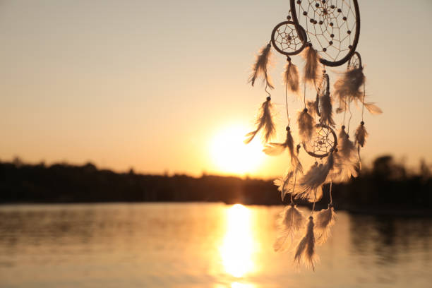 istock Beautiful handmade dream catcher near river at sunset. Space for text 1384610428