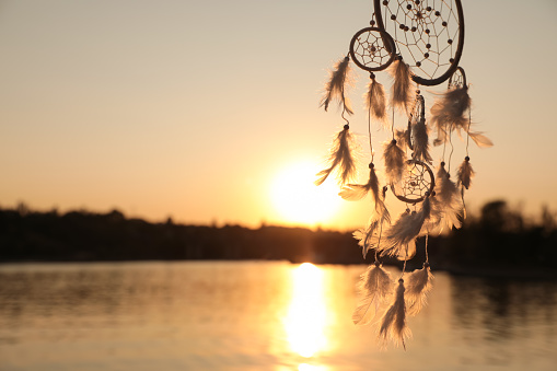 Beautiful handmade dream catcher near river at sunset. Space for text
