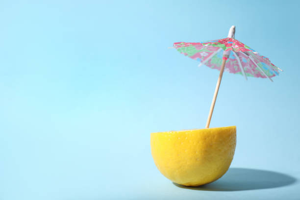 istock Creative image of summer cocktail made with lemon and small paper umbrella on light blue background, space for text 1384610492