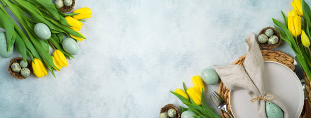 istock Easter festive table setting with easter eggs decoration and yellow tulips flowers on gray background. Top view with copy space 1384610578