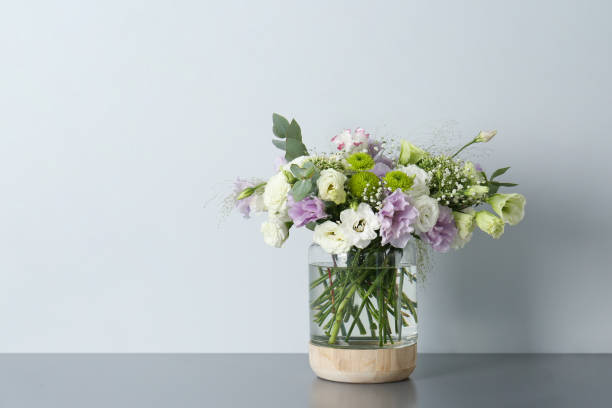 istock Bouquet with beautiful Eustoma flowers in vase on grey table against light background. Space for text 1384611781