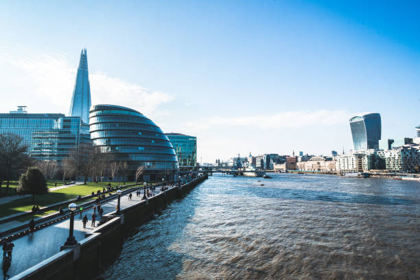 Tourists and locals walking on the riverbank of Thames. City hall on the left.