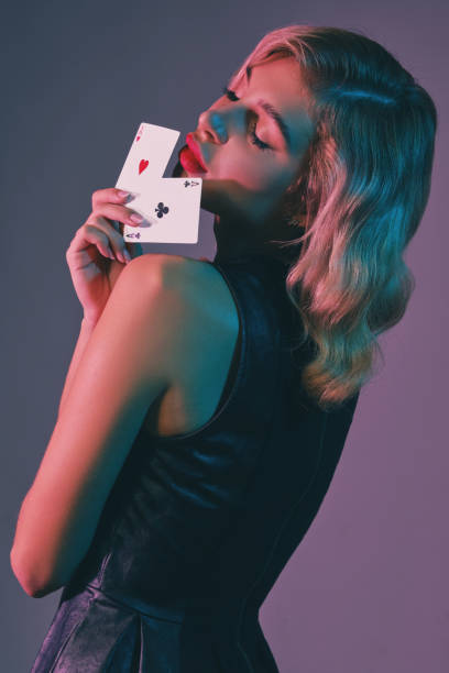 blondynka w czarnej stylowej sukience pokazująca dwie karty do gry, pozując na kolorowym tle. rozrywka hazardowa, poker, kasyno. zbliżenie - casino black and white gambling chip gambling zdjęcia i obrazy z banku zdjęć