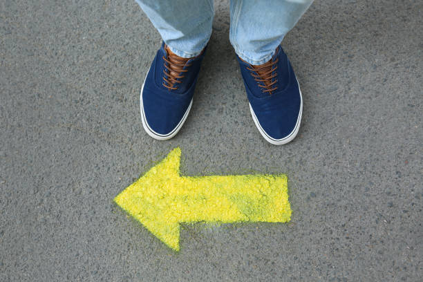 istock Man standing near arrow on asphalt, top view 1384612424
