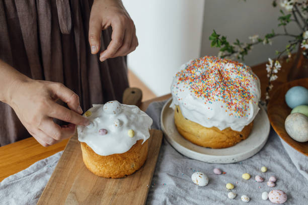 femme décorant du pain de pâques fait maison avec un glaçage au sucre et des œufs de bonbons sur une table rustique. joyeuses pâques! femme cuisinant un gâteau de pâques élégant avec du glaçage et des saupoudrages - baking cake making women photos et images de collection