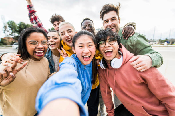 Multiracial friends taking big group selfie shot smiling at camera -Laughing young people standing outdoor and having fun - Cheerful students portrait outside school - Human resources concept stock photo