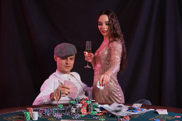 człowiek grający w pokera w kasynie siedzi przy stole ze stosami żetonów, pieniędzy, szampana, kart. świętowanie wygranej z kobietą. czarne tło. zbliżenie - casino black and white gambling chip gambling zdjęcia i obrazy z banku zdjęć