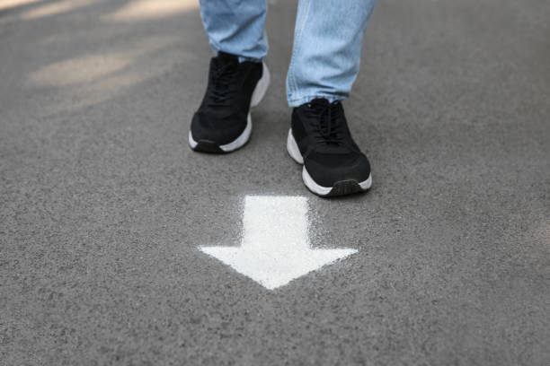 istock Man standing near arrow on asphalt, closeup 1384618556