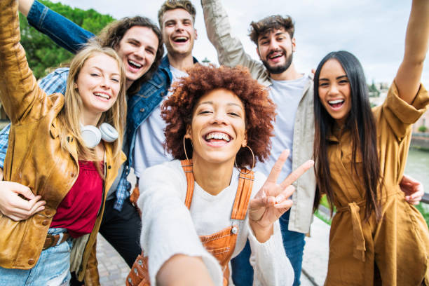 Multiracial group of friends taking selfie pic outside - Happy different young people having fun walking in city center - Youth lifestyle concept with guys and girls enjoying day out together stock photo