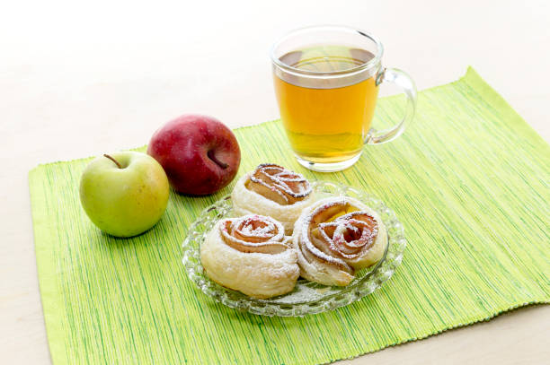 Rosettes from apples in puff pastry, tea and two apples on a table close-up