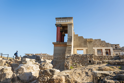 Knossos, Crete, Greece - June the 30th, 2021: Tourists visiting the ruins of the north entrance of the Palace of Knossos, side view of the entrance with famous columns