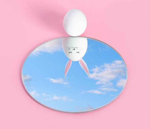 Happy Easter holiday. A white egg on a pink background looks in the mirror and sees a reflection of itself with easter bunny a backdrop of a peaceful sky. Close the sky