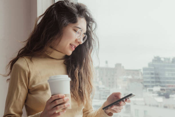 istock Young woman using her mobile while having a coffee in her hotel room. Travel concept. Coffee concept. 1384629306