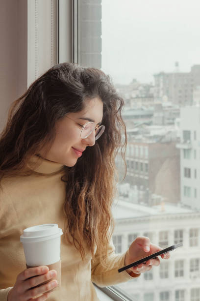 istock Young woman using her mobile while having a coffee in her hotel room. Travel concept. Coffee concept. 1384629321