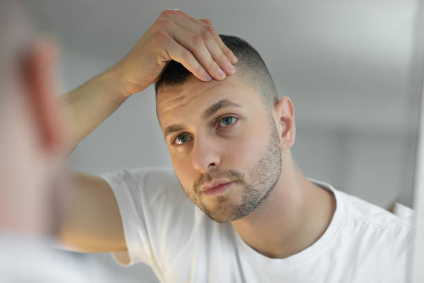 hombre revisando la cara en el espejo - mano en el cabello fotografías e imágenes de stock