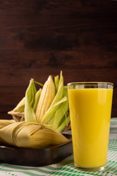 Brazilian corn snack pamonha, corn and corn juice arranged on a table with green and white tablecloth, dark background, selective focus.