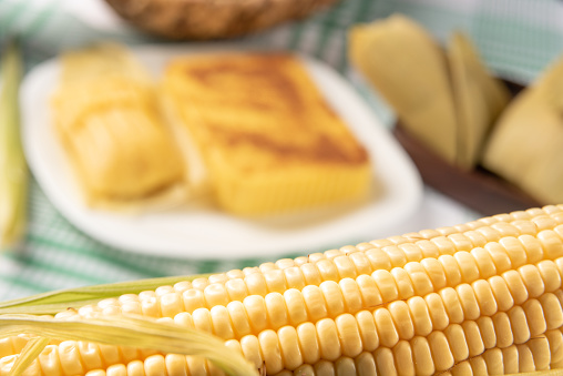Brazilian Cural, candy corn and pamonha, corn on the cob arranged on a table with a green and white tablecloth, dark background, selective focus.