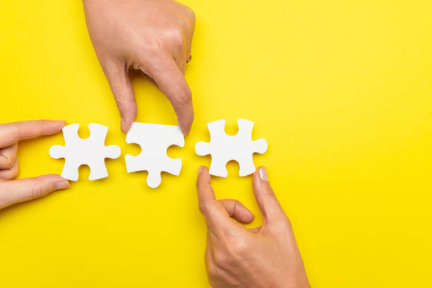Business Teamwork Three hands are holding three puzzle pieces next to another  in front of yellow background. three people stock pictures, royalty-free photos & images