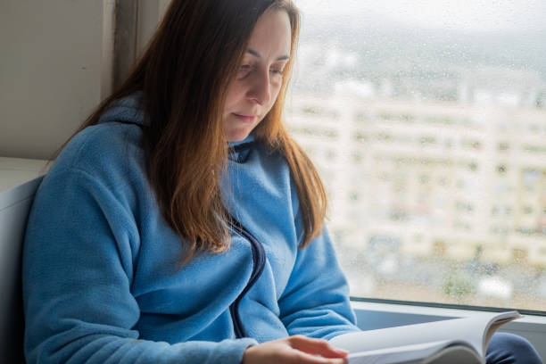 istock woman reading a book by the window 1384652061