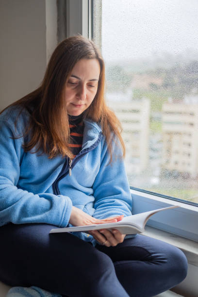istock woman reading a book by the window 1384652147