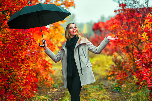 Beautiful girl in gray coat standing near colorful autumn leaves with umbrella.