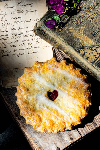 baked cherry pie with antique cook book Antique cook book with dried red roses, handwritten recipe on vintage paper and small baked cherry pie with heart shape in pastry crust cottagecore stock pictures, royalty-free photos & images