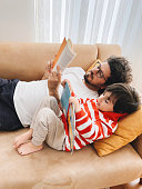 istock Father and son lying on sofa at home and reading book together 1384654894